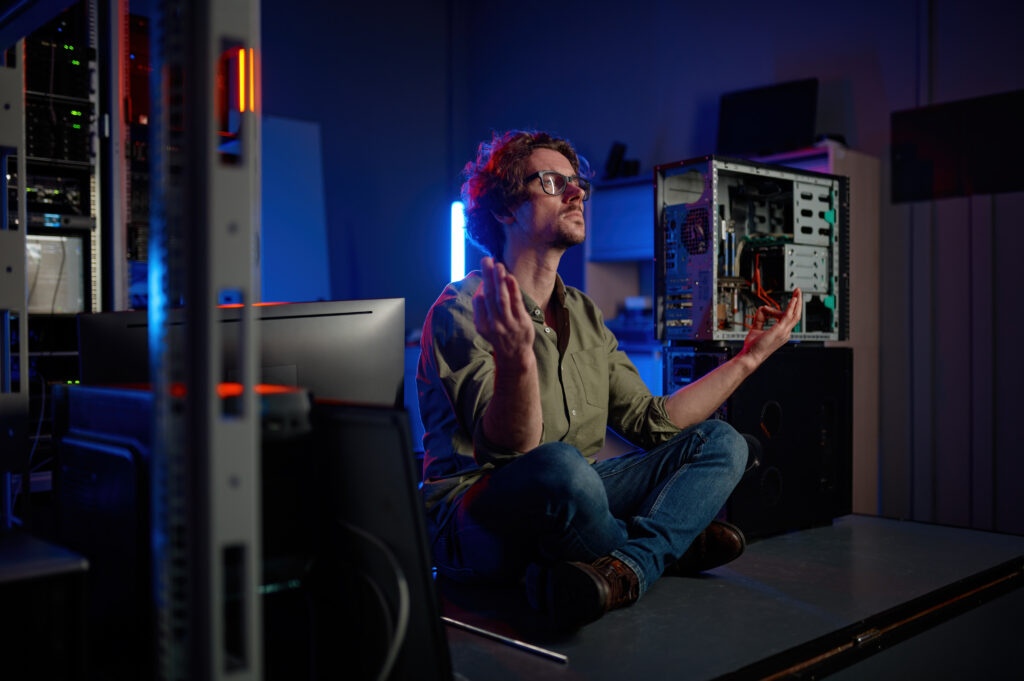 Pensive technician meditating taking breath during work in server room at modern data center. Male installer working with modern equipment for internet connection or mining farm facilities